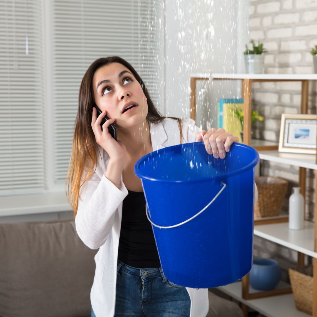 woman holding bucket under leak on phone